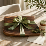 Eaglecreek Boards live edge black walnut wooden board tied with a green ribbon, presented as a gift on a wooden table.
