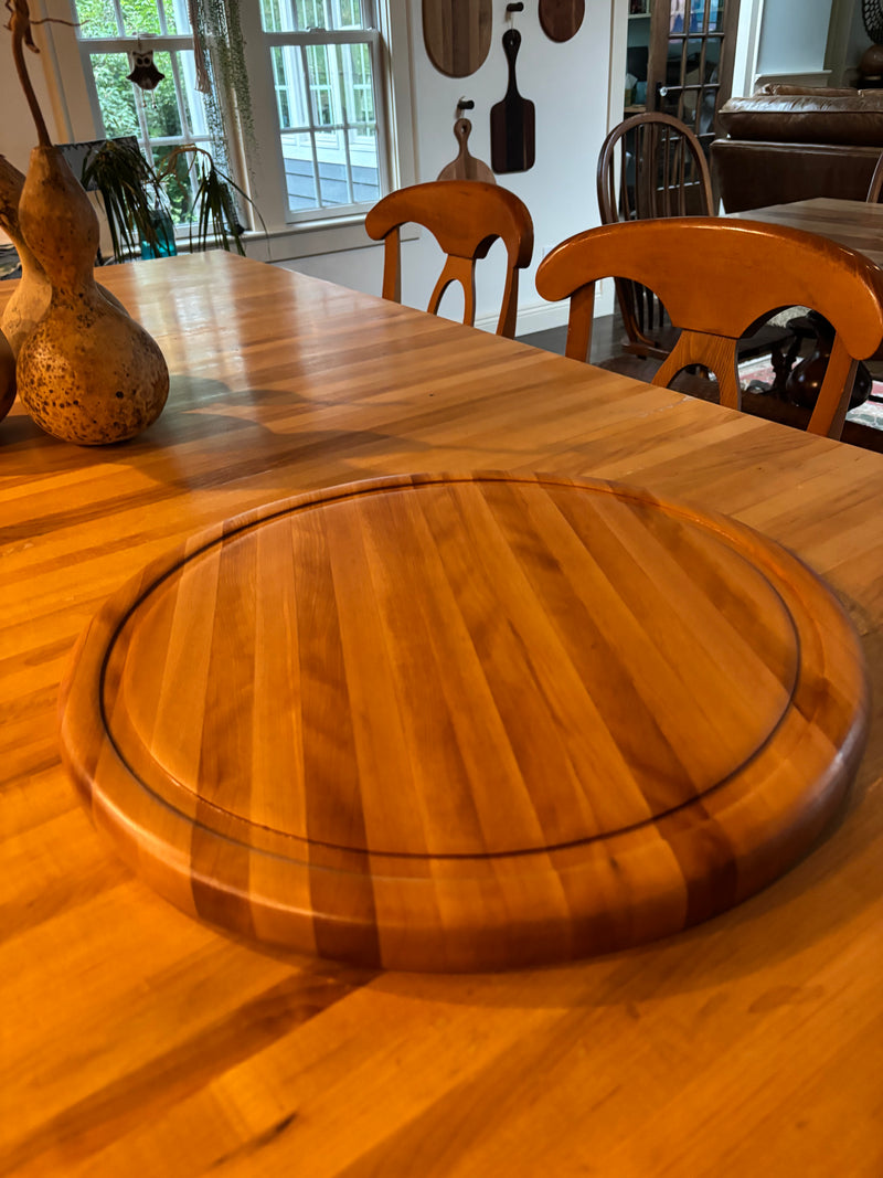 Wooden dining table with a round wooden cutting board in a kitchen setting.
