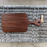 Eaglecreek Boards walnut wood paddle cutting board for serving charcuterie on a grey wicker background