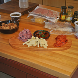 Eaglecreek Boards oval hardwood serving board topped with salami cubes, cheese sticks, and pepperoni slices.